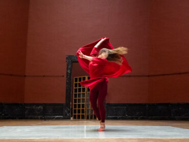 Une danseuse en robe rouge tourbillonne seule sur scène