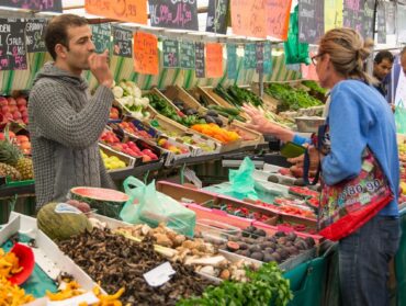 Une cliente devant un étal de marché en train de choisir fruits et légumes.