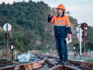 Un homme en tenue de chantier parle au talkie-walkie debout sur un aiguillage de train