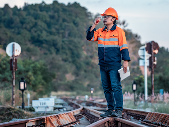 Un homme en tenue de chantier parle au talkie-walkie debout sur un aiguillage de train